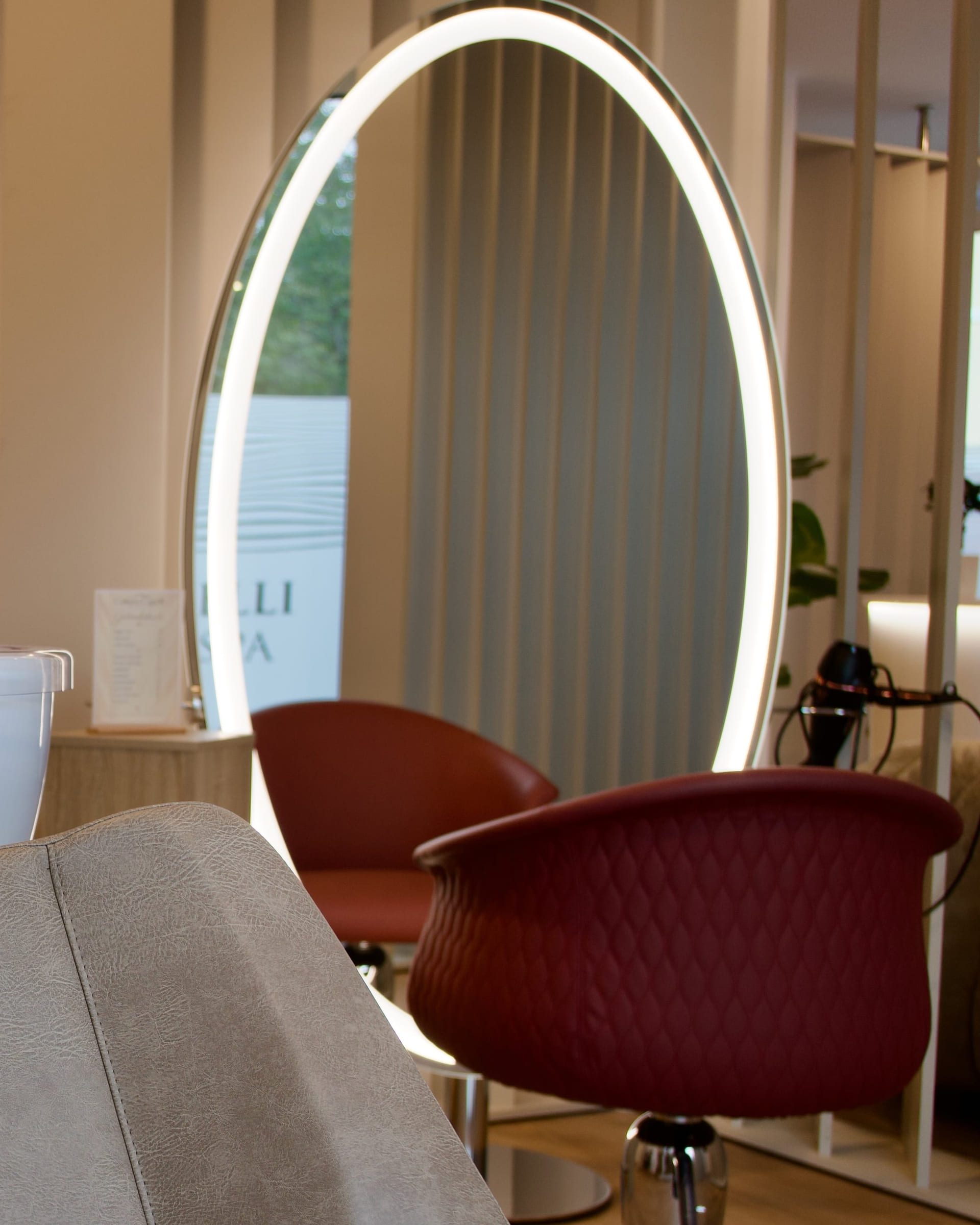Beleuchteter ovaler Spiegel und rote Friseursessel in der Kabine
